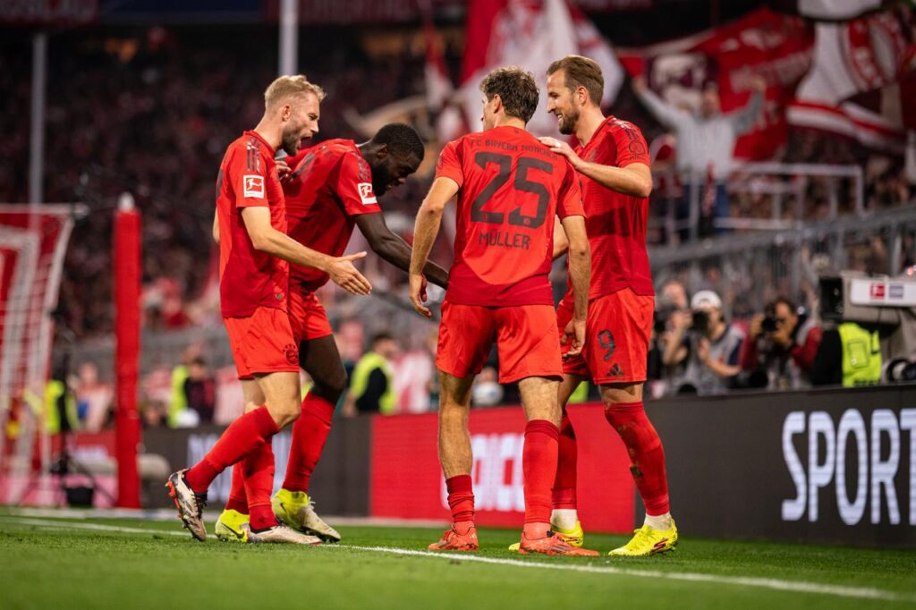 Spieler des FC Bayern München jubeln gemeinsam im Stadion Allianz Arena in München, Deutschland. Im Hintergrund Fotografen und Fans mit Fahnen.